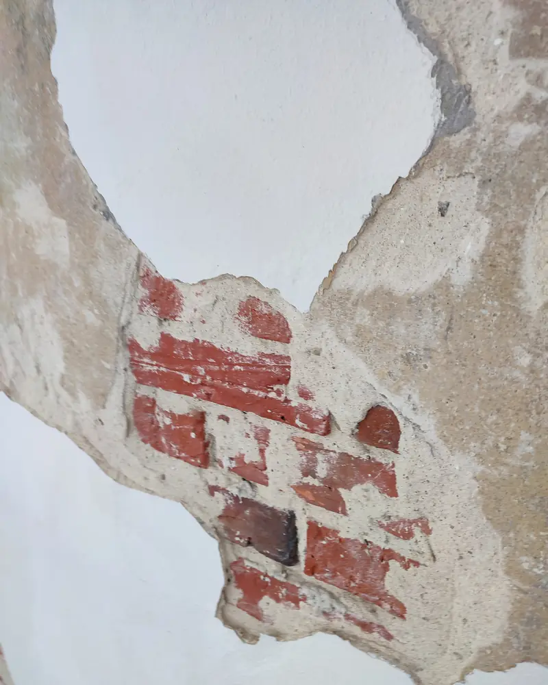 Abgeplatzter Anstrich und Putz, darunter freiliegendes rotes Ziegelmauerwerk