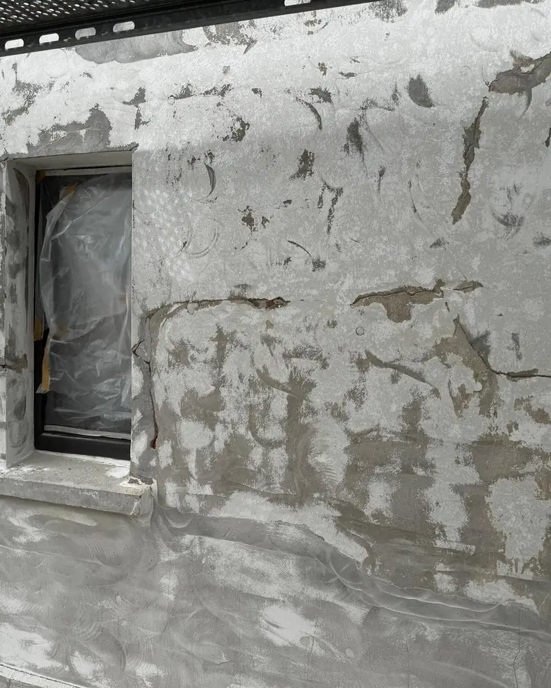 Wandfläche um ein Fenster nach dem Abtragen des Altanstrichs, Putz mit Rissen und Fehlstellen